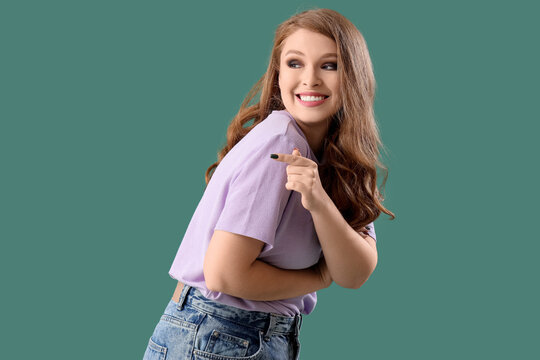 Young gossip woman pointing at something on green background