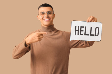 Handsome young man pointing at speech bubble with word HELLO on brown background © Pixel-Shot