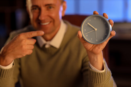 Mature man pointing at alarm clock in office, closeup