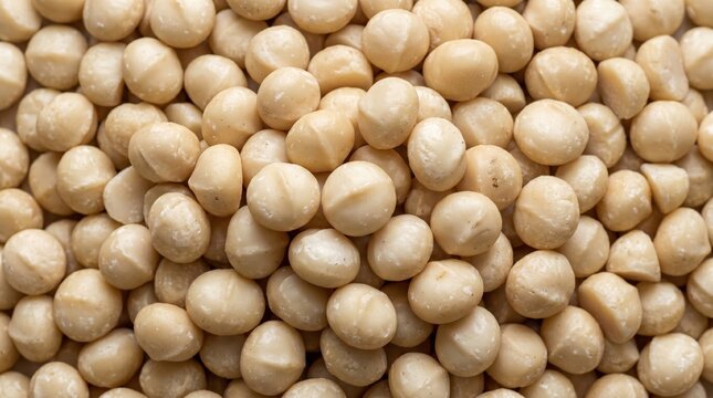 A close-up overhead view of a large pile of shelled macadamia nuts showcasing their smooth creamy white texture and round shape filling the entire frame