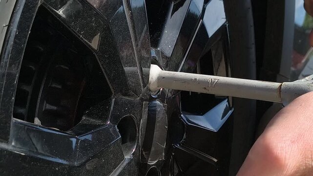 Close-up of mechanic loosening car wheel bolts with lug wrench on alloy rim outdoors, showing automotive maintenance, tire replacement, repair process, and vehicle service