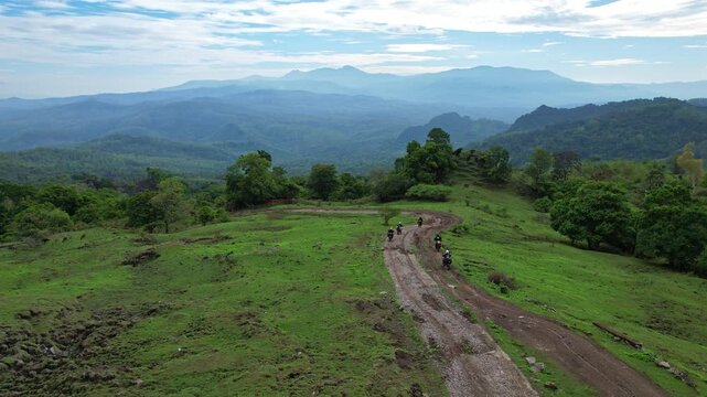 Aerial drone footage of trail motorbike riders going thru a dirt and muddy agricultural path, with holes and bumps, in Kupang regency, Timor island, Indonesia, with forests and mountains around