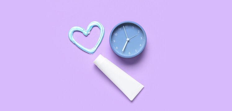 Heart made of toothpaste and clock on lilac background