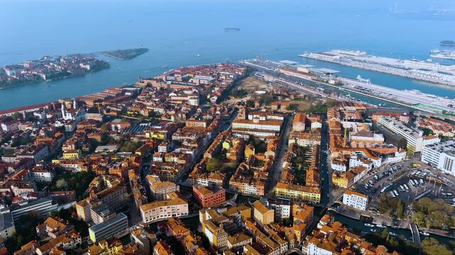 4K aerial view of Venice Santa Croce district with Piazzale Roma, Maritime Station cruise terminals, terracotta rooftops and Venetian lagoon stretching toward the mainland at golden hour.