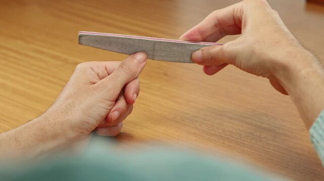 Closeup image of a female filing her fingernails with a black cardboard nail file during a manicure routine.