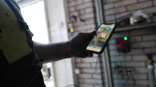 Skilled automotive technician in a garage, checking vehicle repair details on smartphone, showcasing modern technology integration in automotive service workflow and communication