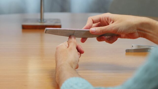 Young woman filing her fingernails with a black emery board during a personal manicure and beauty routine indoors.