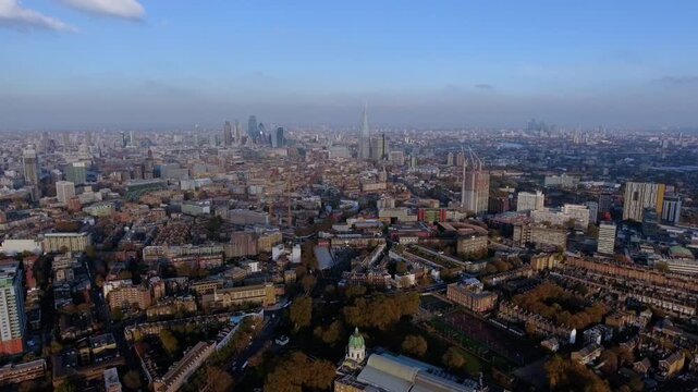 4K aerial view of Imperial War Museum with green dome in South London with City of London skyscrapers, The Shard, Canary Wharf and autumn foliage stretching to the horizon.