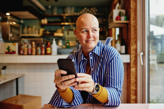 Smiling woman in a blue striped shirt uses smartphone at a cafe, capturing a relaxed moment