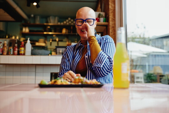 Smiling bald woman with blue glasses enjoying a meal at a cafe table