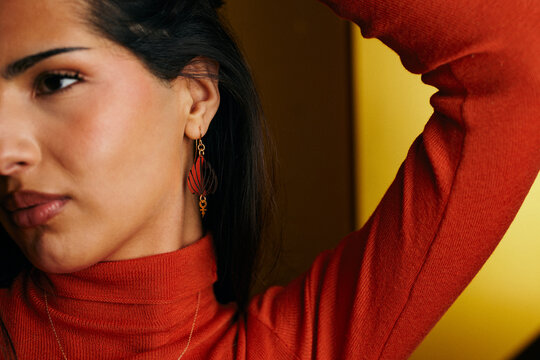 Portrait of a woman wearing statement earrings and a red turtleneck against a warm background