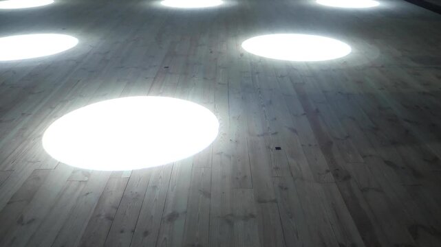 Flashing colorful spotlights and moving bright white beams sweep across dark wooden stage floor creating dramatic theatrical atmosphere for live performance background during concert setup.