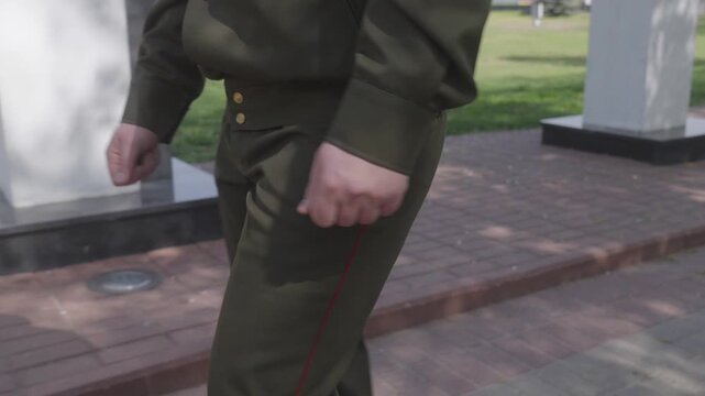 Detailed side perspective captures male military personnel mid stride wearing traditional khaki tunic with golden buttons and trousers featuring distinct red side stripes