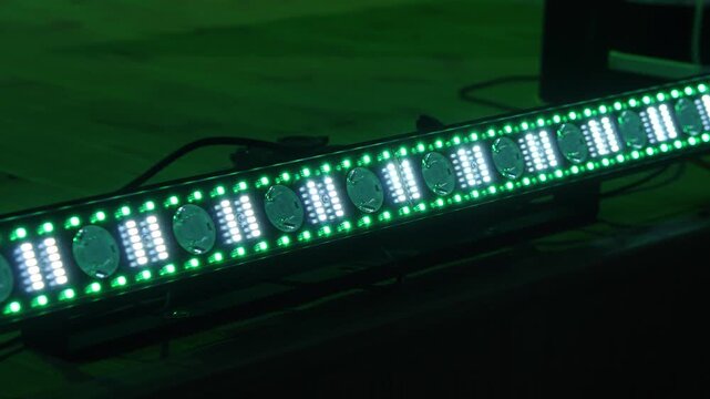 Linear professional stage lighting fixture flashing rhythmic green led patterns and bright white strobe effects on floor during theatrical concert production setup.