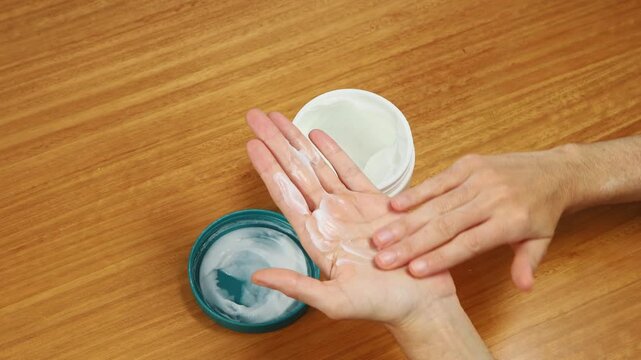 Young woman applying petroleum jelly on her hands to moisturize and protect dry skin during a skincare routine.