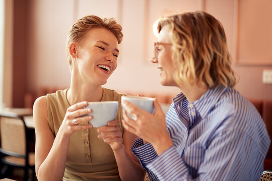 Two women laughing over coffee in a cozy cafe, enjoying a friendly conversation