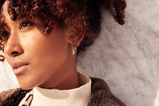 Close-up portrait of a stylish black strong woman with curly hair wearing a beige turtleneck and brown coat