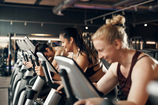 Smiling group of fit young diverse women in sportswear riding on stationary bikes during a cardio workout class together in a health club