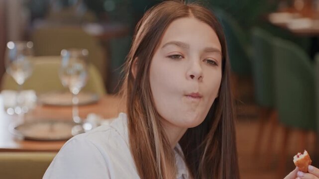 Young woman tasting pastry in restaurant thoughtful expression, upscale table with glassware and green chairs, slow chew and subtle disappointment, cinematic warm light, closeup portrait of teen diner