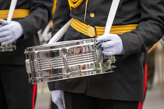 Uniformed soldier in white gloves holds polished silver metallic snare drum featuring yellow ceremonial belt and golden buckle during festive parade.