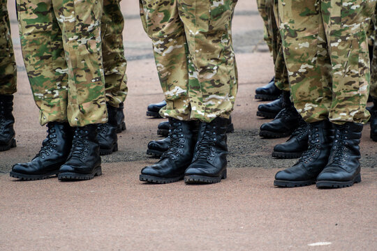 Low angle view soldiers wearing multicam camouflage pants and black leather tactical boots standing in row on asphalt during military parade or outdoor training exercise