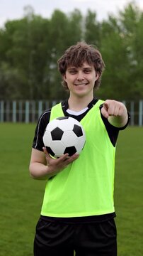 Young smiling man football player holding soccer ball pointing with finger to the camera and to you. Vertical video.