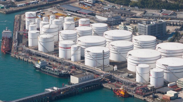 Aerial view of large white industrial oil storage tanks at a fuel terminal on the waterfront with cargo ships docked at the pier Hong Kong, Hong Kong.