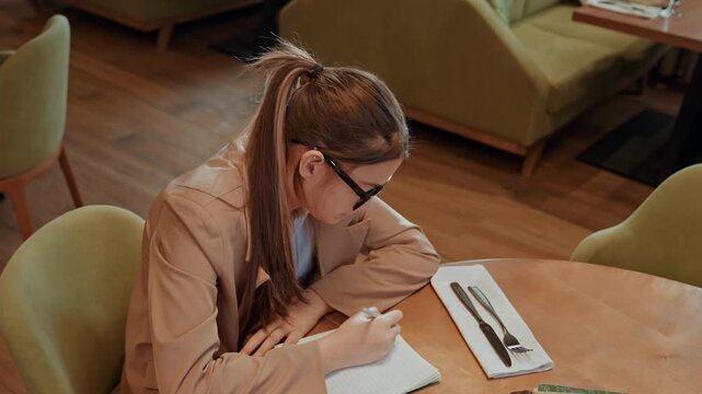 Gentle woman notes serenely outdoors. Tranquil scene where lady thoughtfully writes outside surrounded by nature. Peaceful woman diligently capturing her ideas in lush garden environment