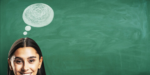 Smiling woman with thought bubble drawn on green chalkboard background suggesting ideas and creativity for education concept poster banner. © Who is Danny