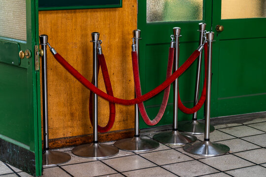 Red velvet rope barriers with chrome stanchions inside a heritage railway carriage or station exhibit, showing vintage train doors, tiled floor, and classic transport museum atmosphere.