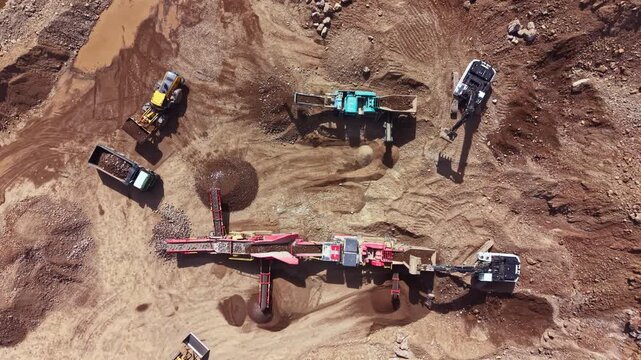 Multiple machines are actively working in a gravel pit. Trucks transport materials while excavators and other equipment process gravel. The scene shows an ongoing construction project.