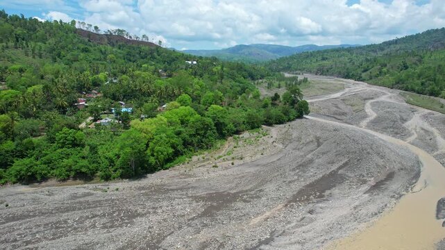 Aerial drone footage of Noebesi dry river and it's village nearby, with many stones, low water lever, and many hills and forests behind, in South Timor regency, Timor, Indonesia
