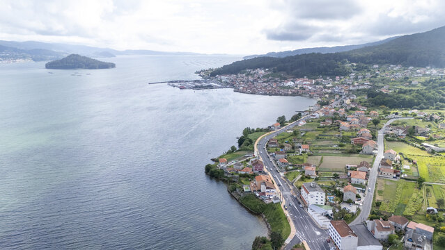 Aerial view of the coastal town of Casalvito featuring traditional houses and a winding road along the blue waters of the bay under a cloudy sky Casalvito, Pontevedra, Spain.