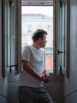Portrait of a pensive man standing by an open wooden window in a European apartment