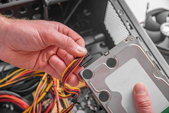 A male technician is connecting a SATA power cable to a hard drive during a computer assembly.