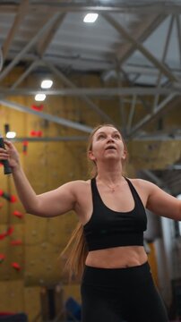 White woman executing badminton smash overhead during dynamic indoor rally, focused gaze and athletic core strength with long ponytail and gym roof beams in background, energetic match atmosphere