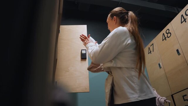 Locker badminton player zips puffer jacket before leaving, quick movements in numbered wooden locker area, focused expression, warm breath, light shadow play, brief celebration and relief after match,