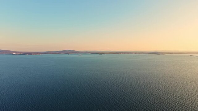 The scene shows a vast sea with gentle waves and distant hills at sunset. The sky shifts from blue to warm colors, marking the end of the day. Ships can be seen on the horizon.