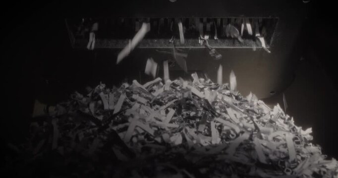 Close up view of a paper shredder destroying confidential documents into small pieces in a dark office room