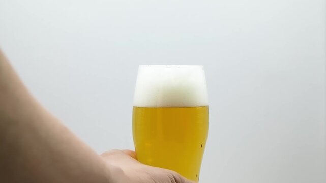 Hand grabbing a glass of cold beer with foam on white background, pulling away to reveal copy space
