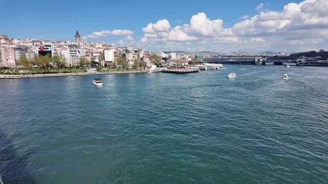 Aerial view of Galata Tower and Karakoy coastline in Istanbul, Turkey, with ferry boats on Golden Horn under blue sky and white clouds, sunny day scenic panoramic shot of historical cityscape.