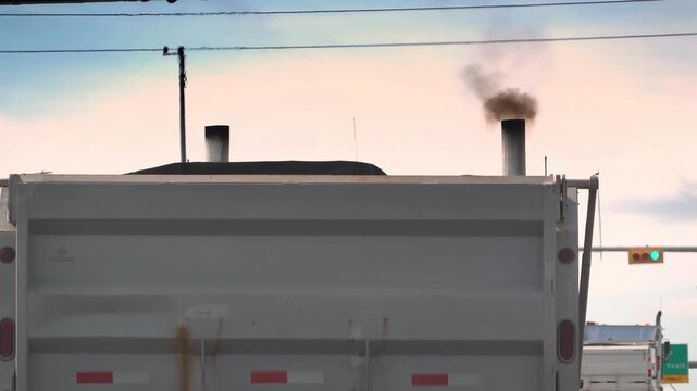 Close-up of heavy black smoke billowing from dual vertical exhaust stacks of a white dump truck.