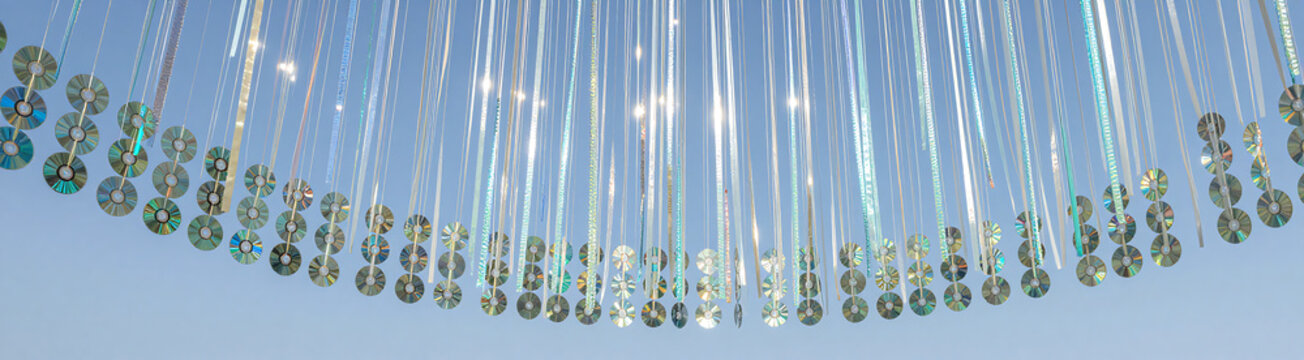 wide shot art installation set bright blue sky shimmering cds iridescent ribbons suspended beneath sprawling canopy