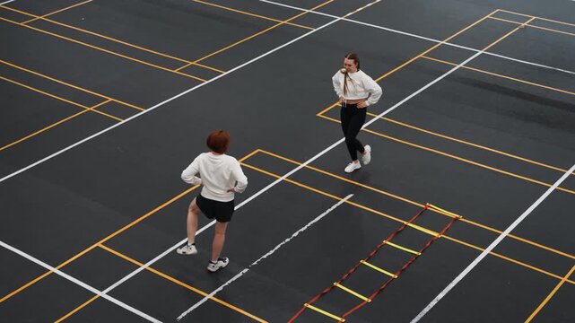 Two players doing badminton footwork drills outdoors, high intensity agility and speed session with lunges and sprints across grid markings, overhead angle captures motion, timing and endurance focus.