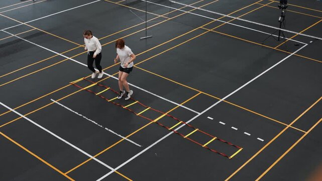 White therapist evaluates badminton footwork on court ladder during clinical assessment, measured steps and gait observation in indoor training hall, focus on mobility strength and injury prevention