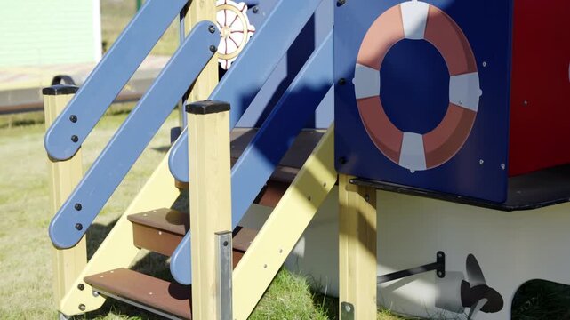 Vibrant multicolored ship structure stands empty on fresh lawn. Red section with white anchor detail stands prominently in sunshine