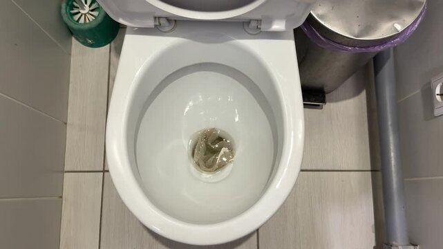 White porcelain toilet bowl stained with urine, overhead view in tiled bathroom showing toilet brush, gray plumbing pipe, used