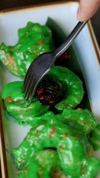Fork pressing green glazed shrimp bite on rectangular dish crispy coating under glossy sauce, chili flakes sprinkle, closeup motion of tasting action, street food energy and playful foodie moment