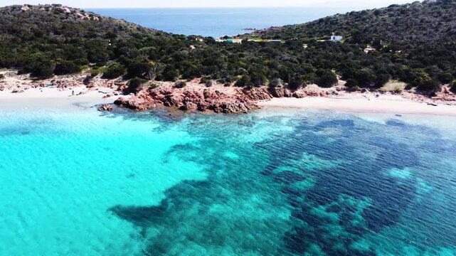 Aerial pull back view moving away from the shore at Capo Coda Cavallo with turquoise sea rocky coastline and Mediterranean landscape in Sardinia