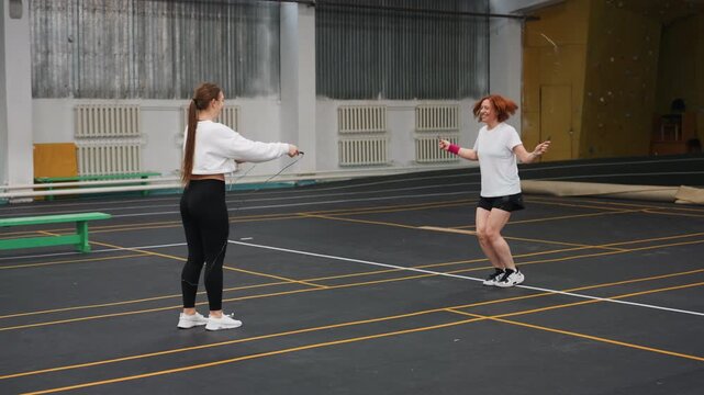Two women practicing precise badminton serves indoor, focused coaching on wrist control and timing, slow deliberate motions and correction of posture on marked court, emphasis on accuracy and rhythm